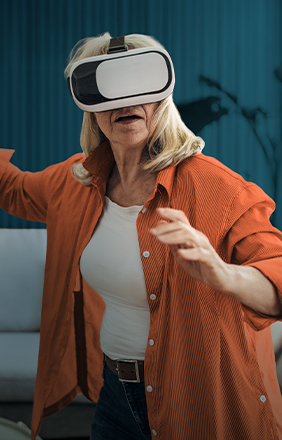 Older woman in orange shirt experiences virtual reality with a headset, appearing fascinated and engaged.