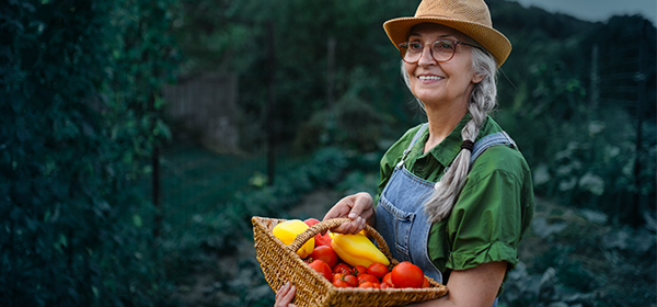 Smiling woman holds a basket of vegetables in a lush garden