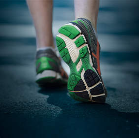 Close-up of a person walking on a road, showing the green and black soles of their running shoes.