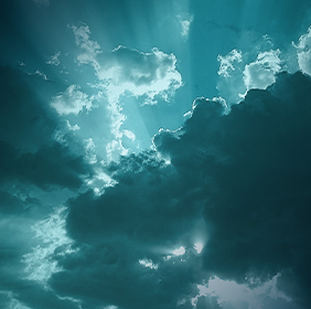 Dark and light clouds with sunbeams shining through, creating a dramatic sky in shades of teal and white.
