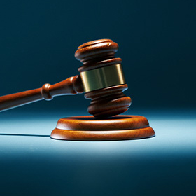An image of a gavel sitting on a table with a blue background.