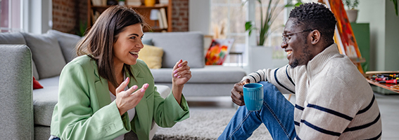 A couple sit on the floor having a conversation.