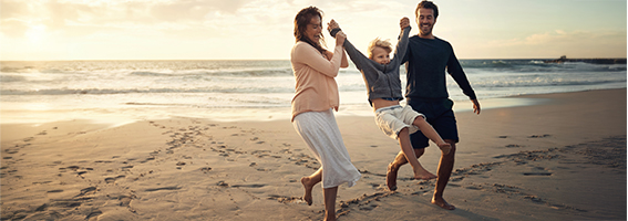 Happy family walk barefoot along a sandy beach at sunset.