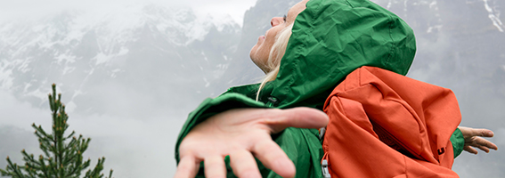 Hiker in a green jacket stretching their arms out in a mountain landscape